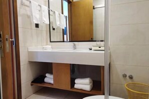 A modern bathroom with a white sink, mirror, and towel rack. There is a wooden shelf below the sink and a yellow basket to the right.
