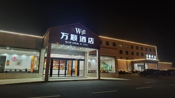 Das Außere des WanShun Hotels mit auffälliger Beschilderung, einem überdachten Eingang und einem Parkplatz.