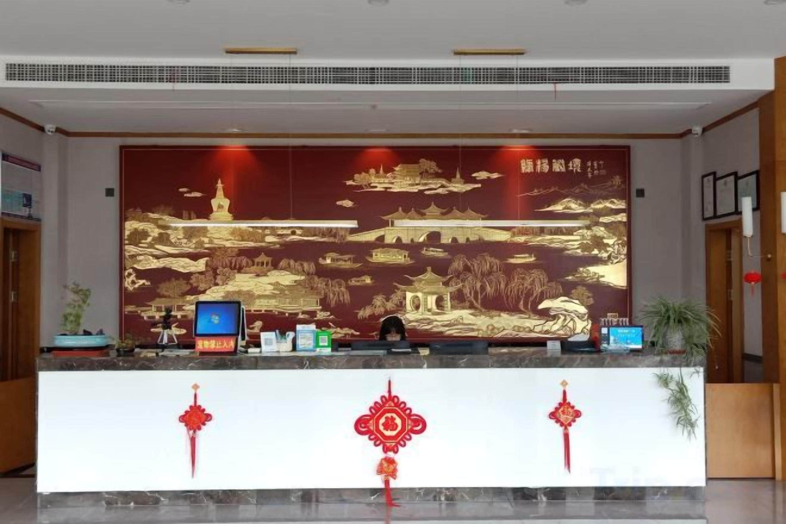 A reception desk with a large decorative wall, a computer, and a plant.