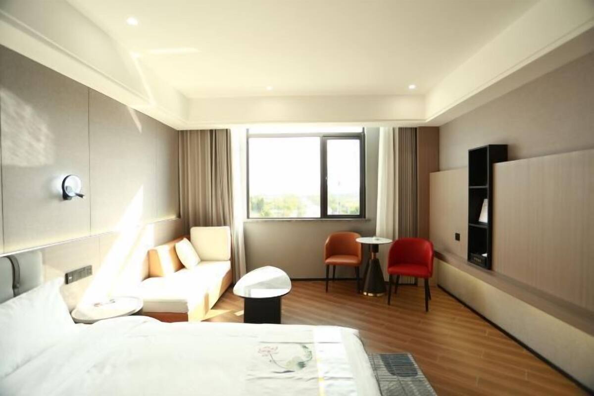 A hotel room with a bed, a sofa, a small table, two chairs, a TV, and a window with curtains.