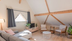 A cozy loft-style living room with a sofa, two armchairs, a TV, and a dining table.