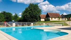 A swimming pool with a fenced deck, surrounded by a grassy area and trees.