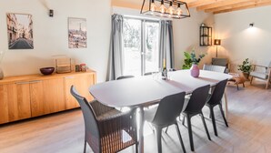 A dining area with a wooden ceiling, a white table, black chairs, and a chandelier.