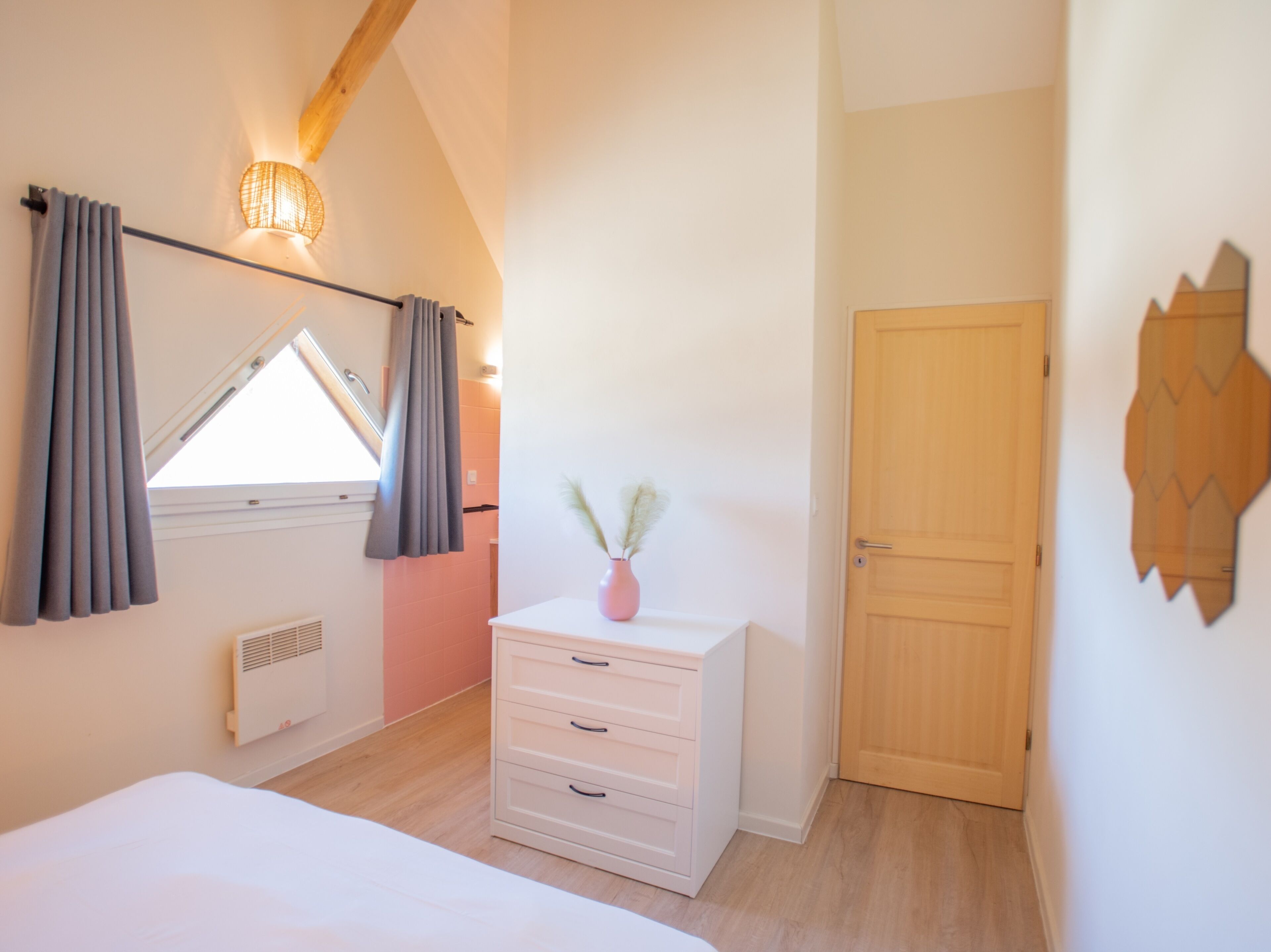 A bedroom with a skylight, a white dresser, a wooden door, and a wall-mounted mirror.