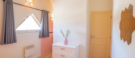 A bedroom with a skylight, a white dresser, a wooden door, and a wall-mounted mirror.
