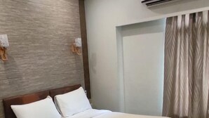 Habitación de hotel con una cama grande, cabecero de madera, unidad de aire acondicionado y cortina en la ventana.