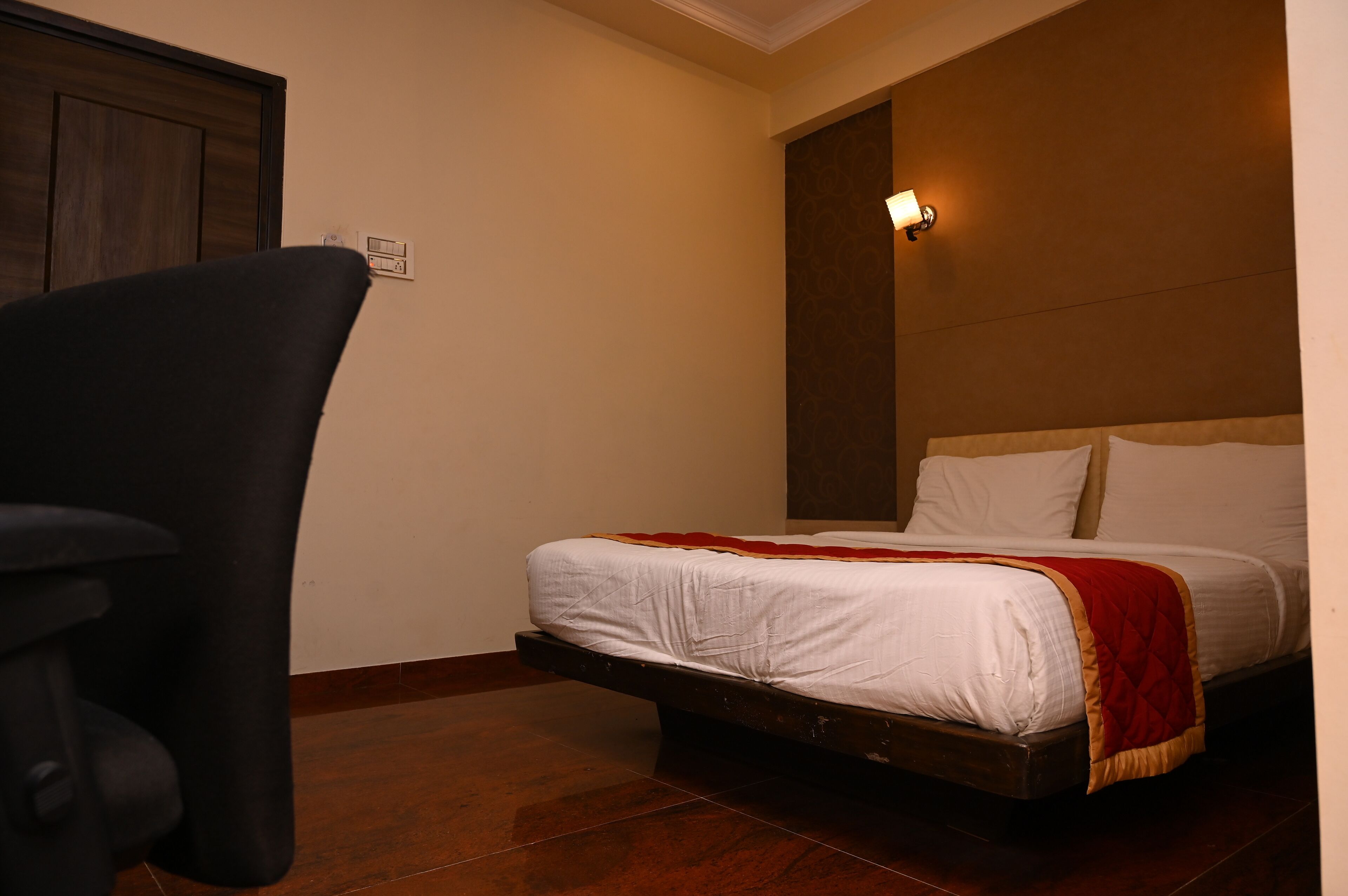 A bedroom with a bed, a chair, and a wall-mounted light fixture.
