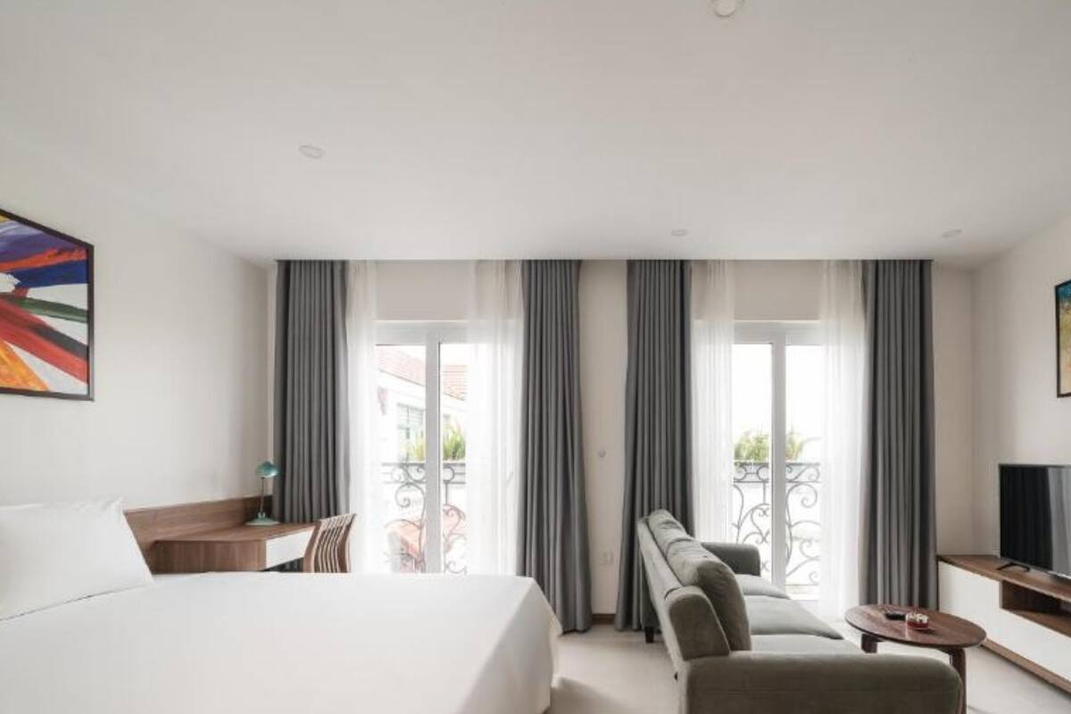 A hotel room with a bed, a sofa, a TV, and a balcony with curtains.