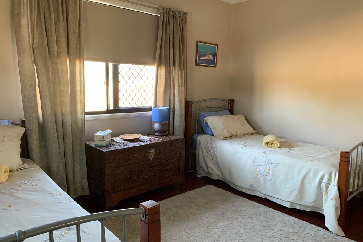 A bedroom with two beds, a wooden dresser, a window with curtains, a bedside lamp, and a framed picture on the wall.