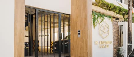 A hotel entrance with a modern design, featuring a staircase leading to the entrance, a gated driveway, and a logo on the wall.