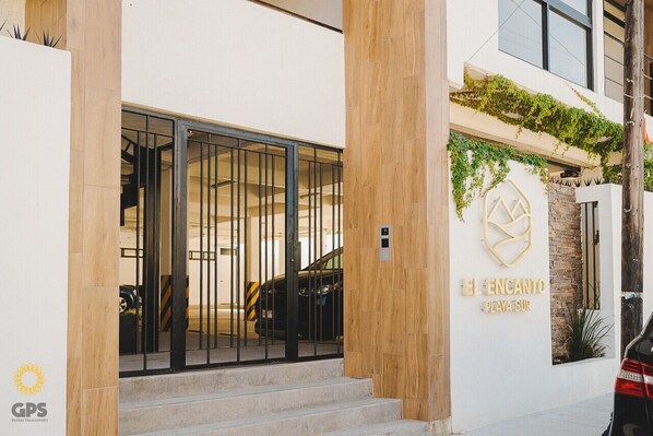 A hotel entrance with a modern design, featuring a staircase leading to the entrance, a gated driveway, and a logo on the wall.