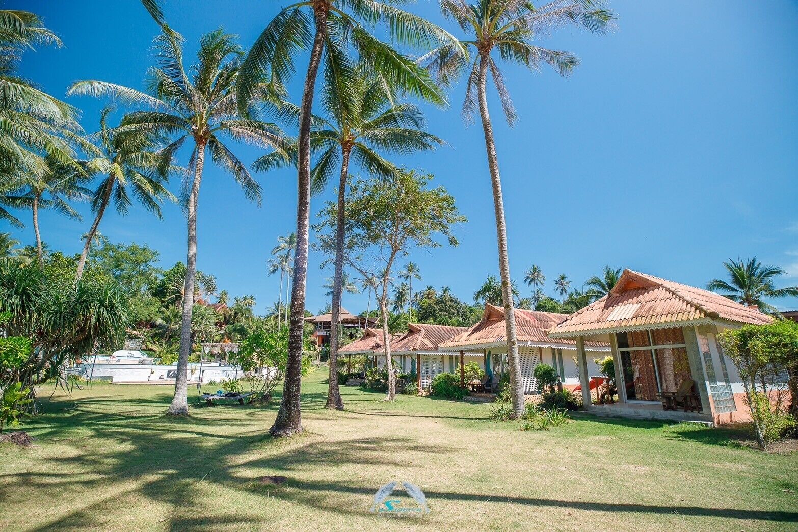 A resort with multiple bungalow-style buildings, surrounded by palm trees and a well-maintained lawn.