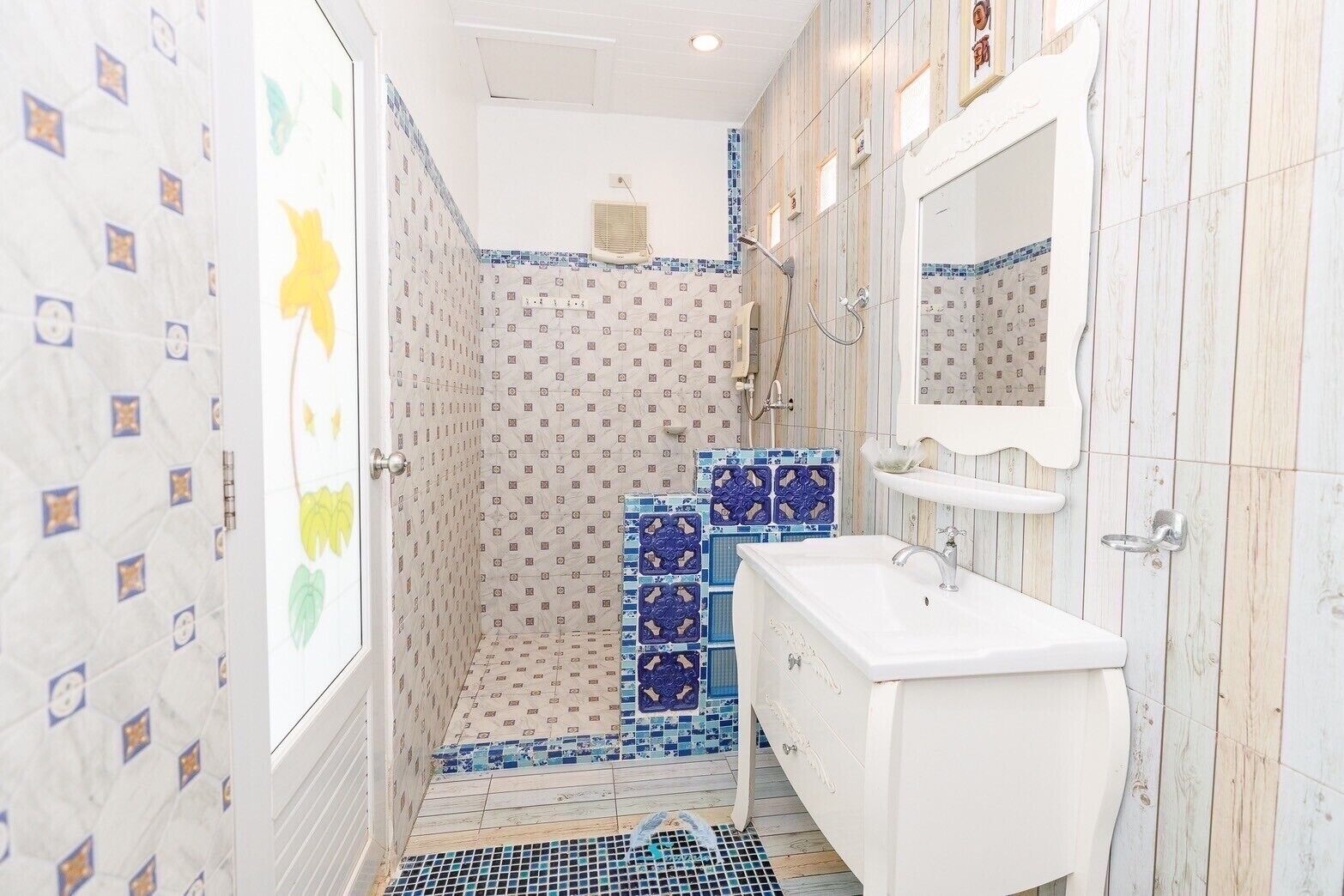 Un baño con azulejos estampados, zona de ducha y un lavabo blanco con espejo.