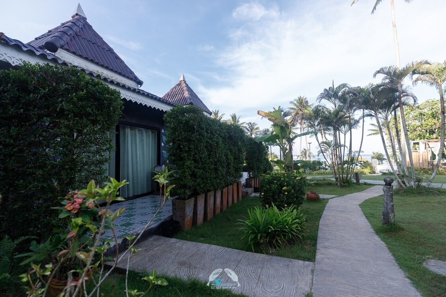 A traditional-style building with a tiled roof and a garden area with palm trees and a pathway.