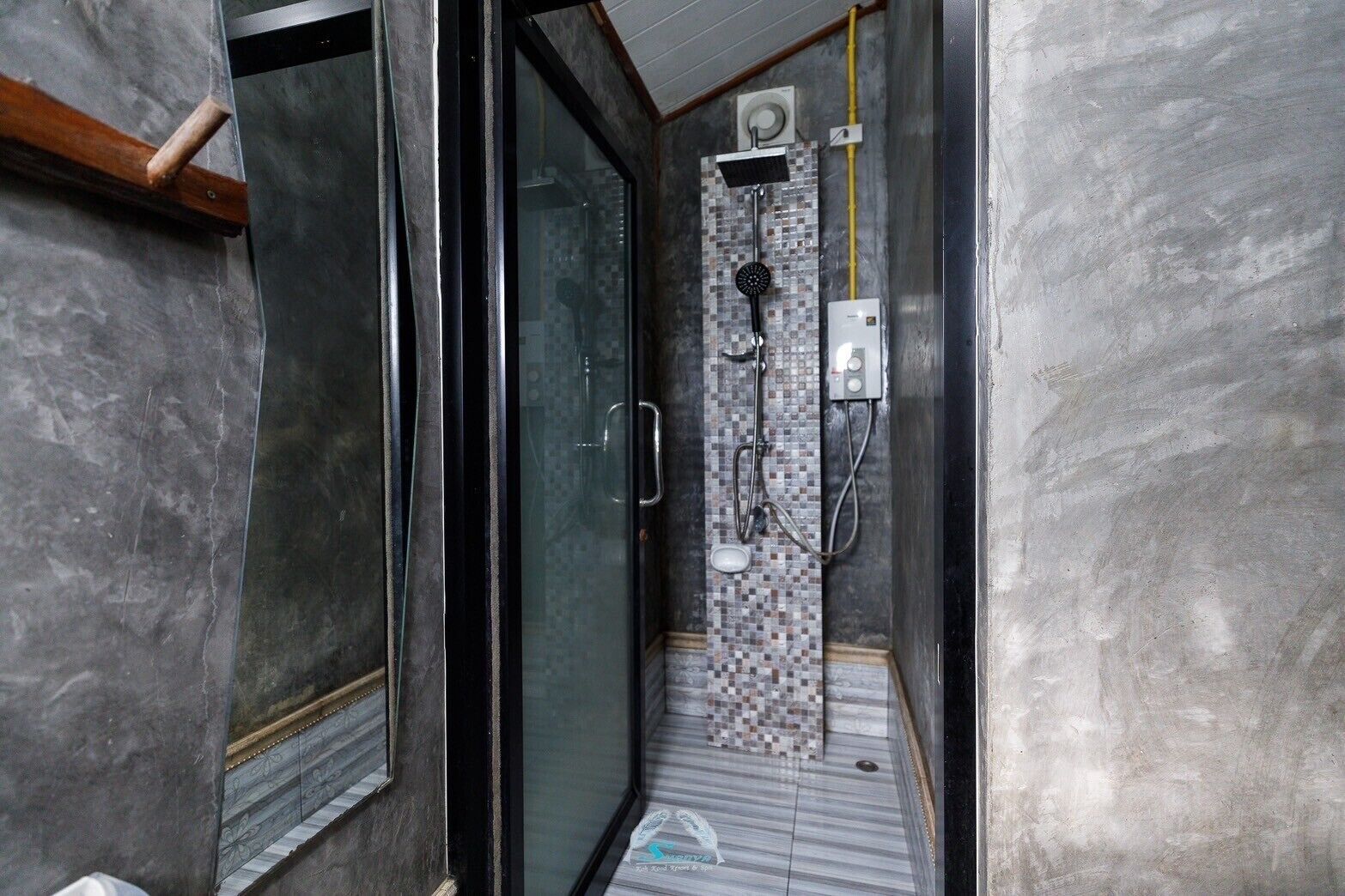 A shower area with a tiled wall, a glass door, and a visible electrical outlet.