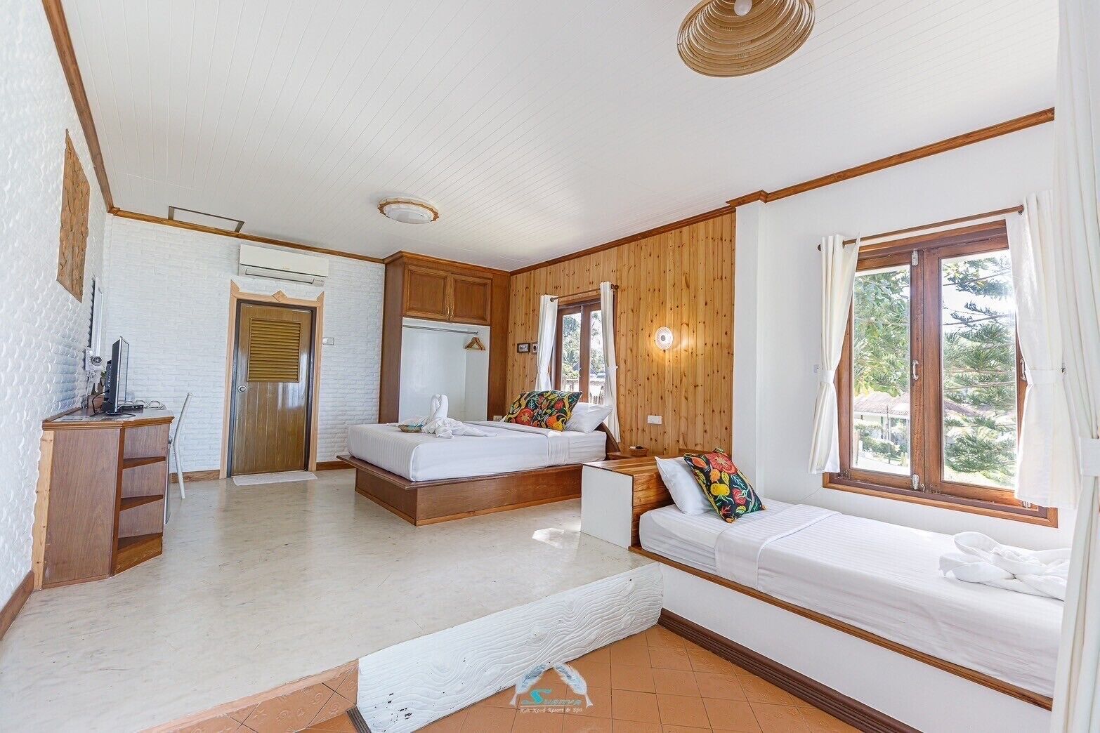 Camera d'albergo con arredamento in legno, un letto, una scrivania con un computer e una finestra vista alberi.