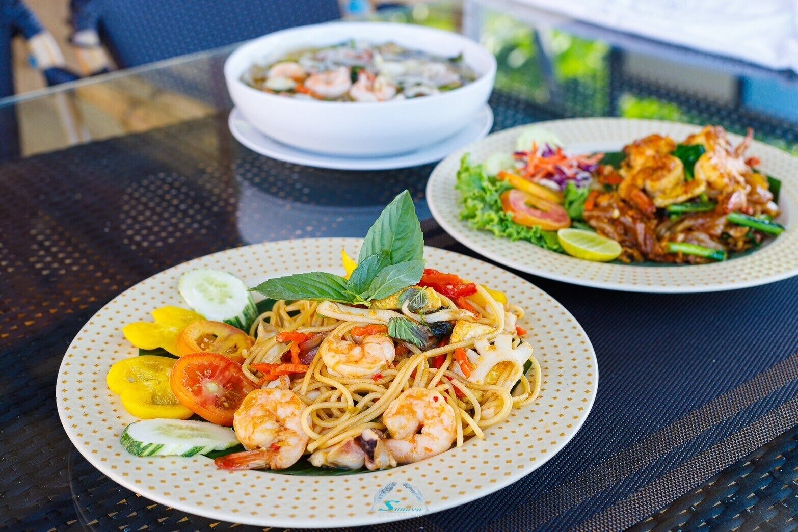 Una mesa con dos platos de comida, uno con fideos y camarones, y otro con ensalada y camarones.