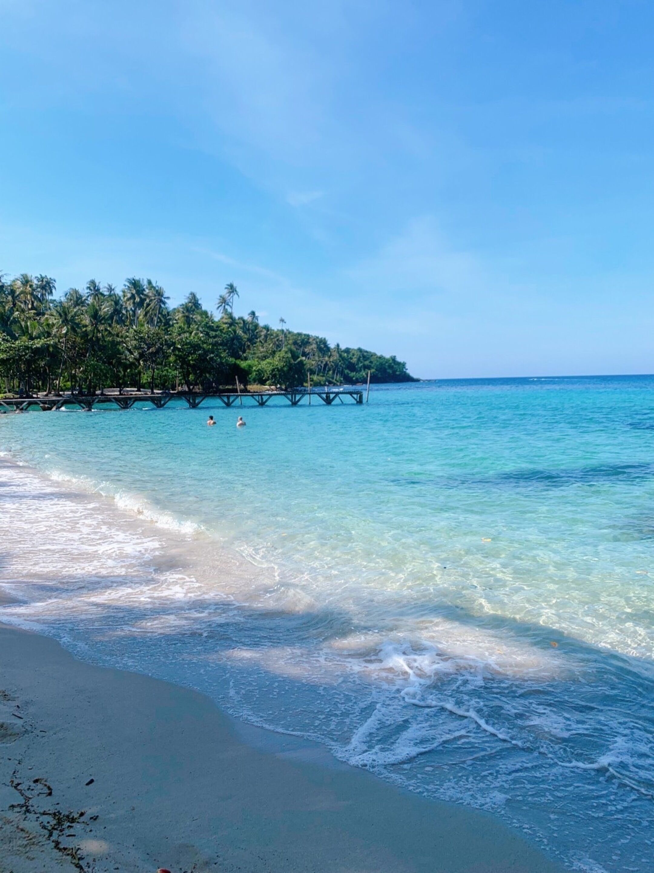 Una playa con agua turquesa cristalina, una orilla arenosa y una isla cubierta de bosque al fondo.