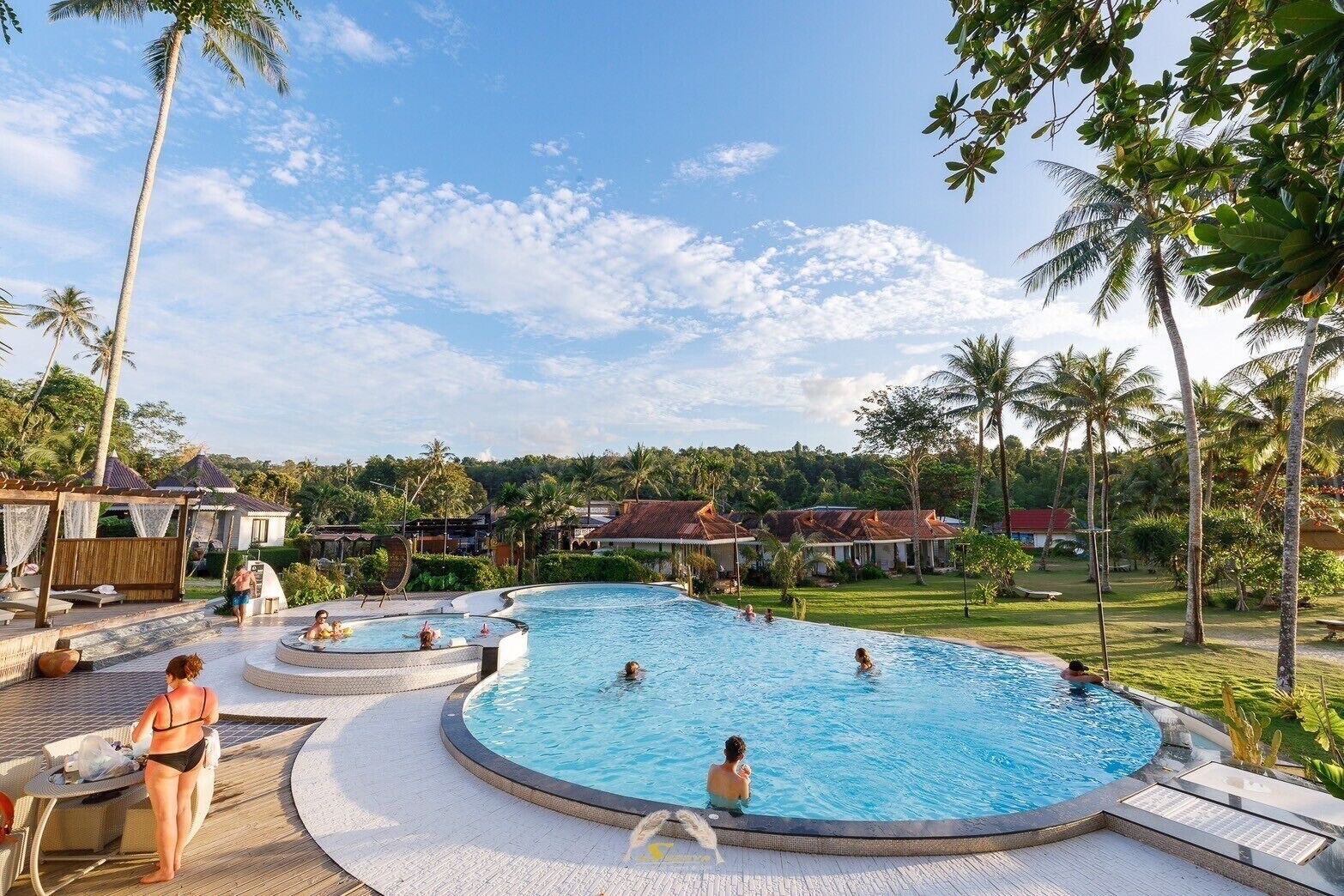 A large outdoor swimming pool surrounded by palm trees and lounge areas.