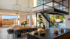 A modern kitchen with a central island, a dining area with chairs, and a staircase leading to an upper level.