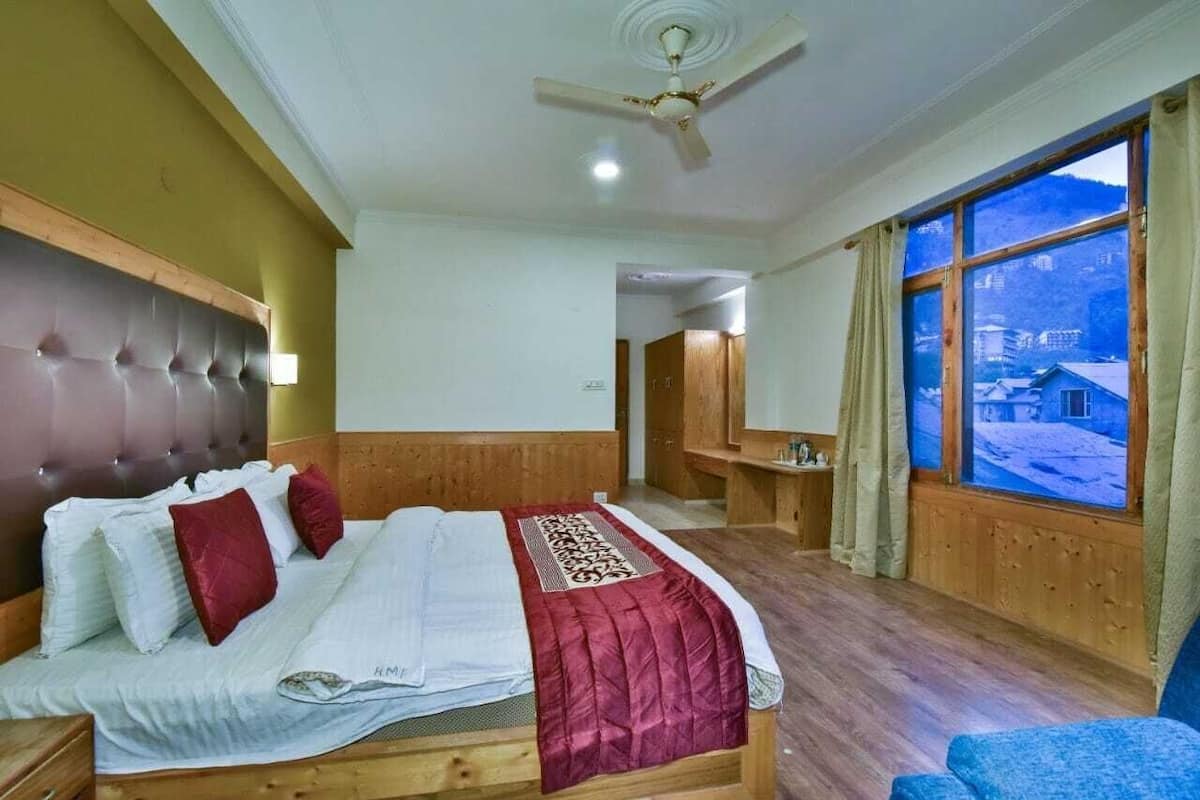 Une chambre à coucher avec un lit, un ventilateur de plafond, une fenêtre donnant sur un beau paysage et une tête de lit en bois.