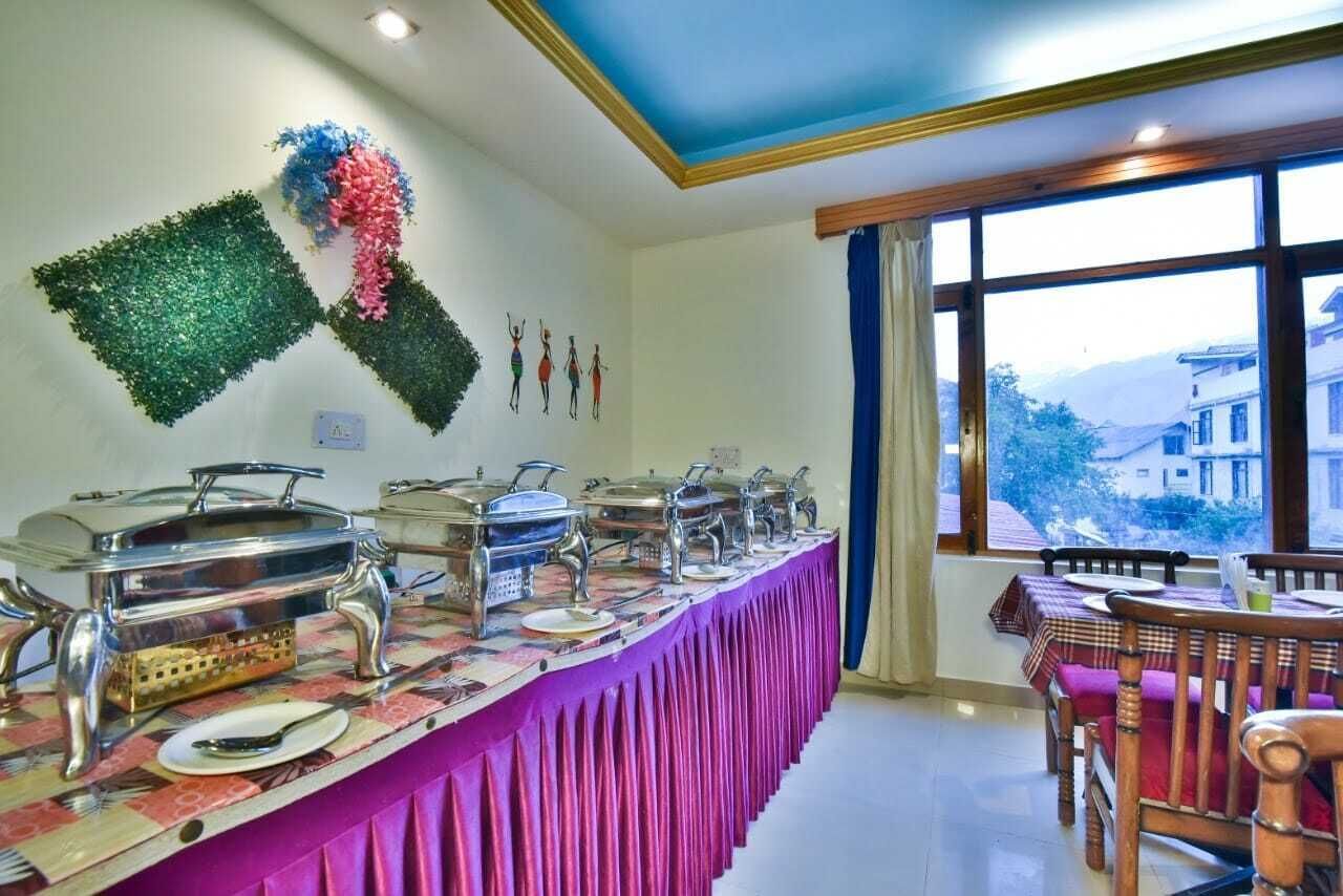 Montaje de bufé con varias estaciones de servicio, una larga mesa con mantel rosa y vistas a un paisaje montañoso a través de grandes ventanales.