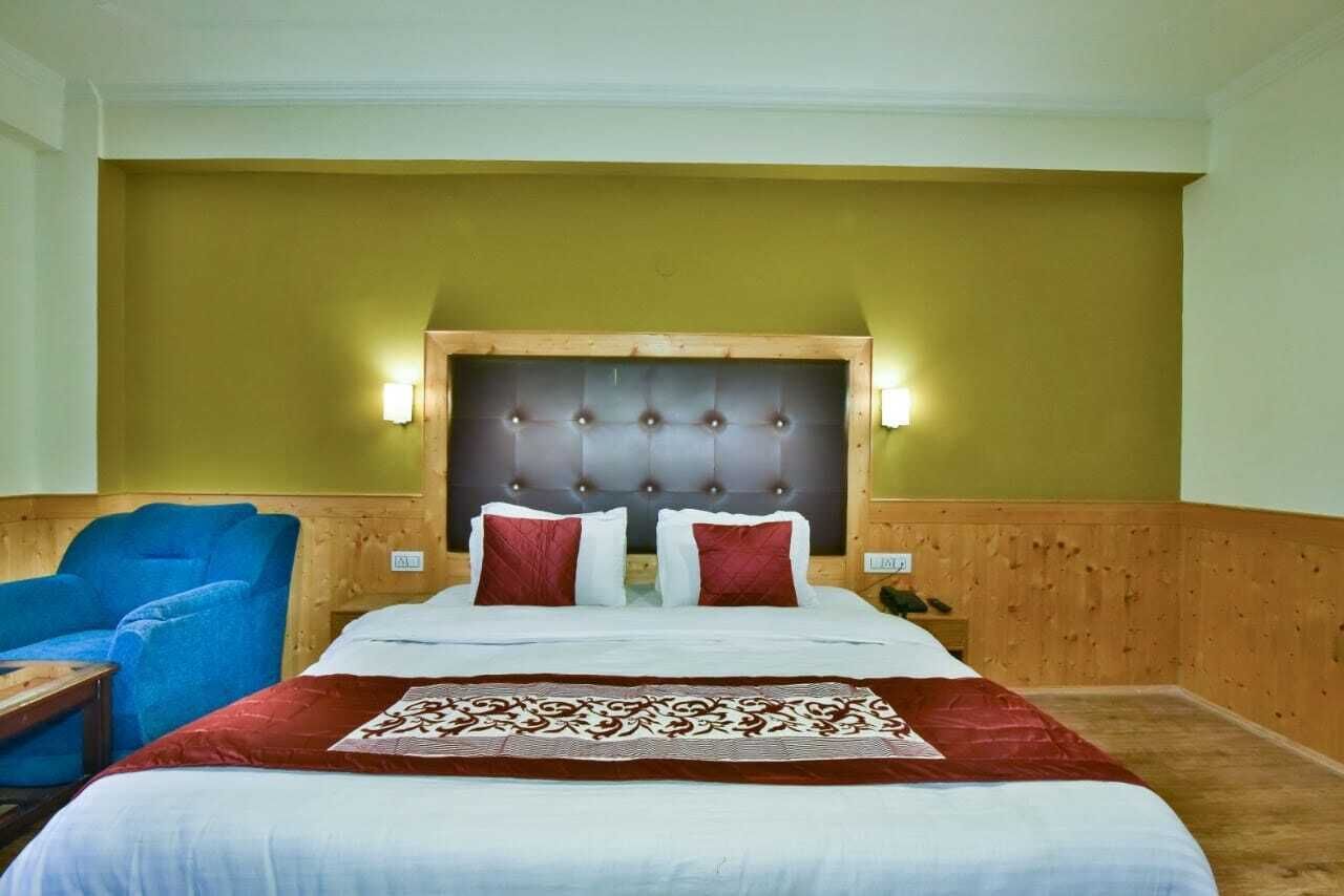 A hotel room with a large bed, two bedside lamps, a wooden headboard, and a blue armchair.