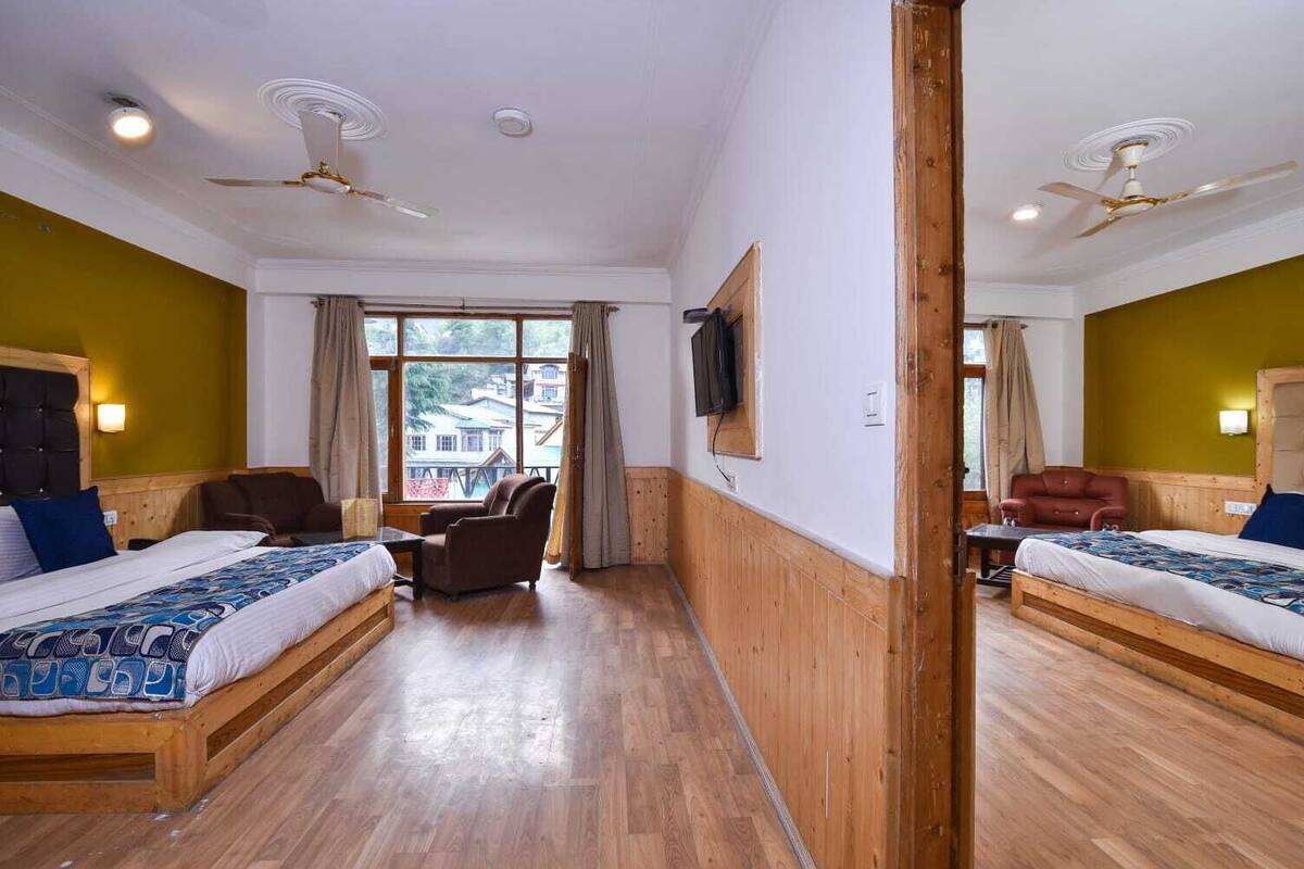 Une chambre d’hôtel avec deux lits, un plancher en bois, une fenêtre avec des rideaux, un téléviseur fixé au mur et un ventilateur de plafond.