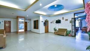 A hotel lobby with a reception desk, a sofa, and a restaurant sign. - Hotel Mukund Palace (Manali)