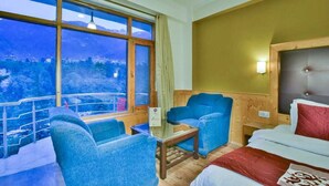A hotel room with a large window offering a mountain view, a bed with a red and white duvet, and two blue armchairs. - Hotel Mukund Palace (Manali)