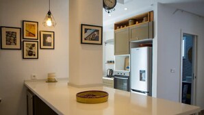 A modern kitchen with white countertops, a built-in oven, and a refrigerator. There are framed pictures on the wall and a basket on the counter. - Peaceful corner in the center of La Marsa (Tunis)