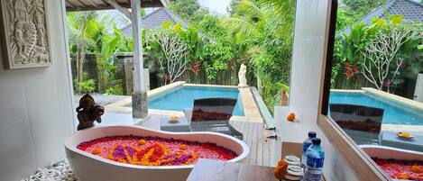 A bathroom with a large bathtub filled with colorful flowers, a wooden bench, and a sink with a mirror.