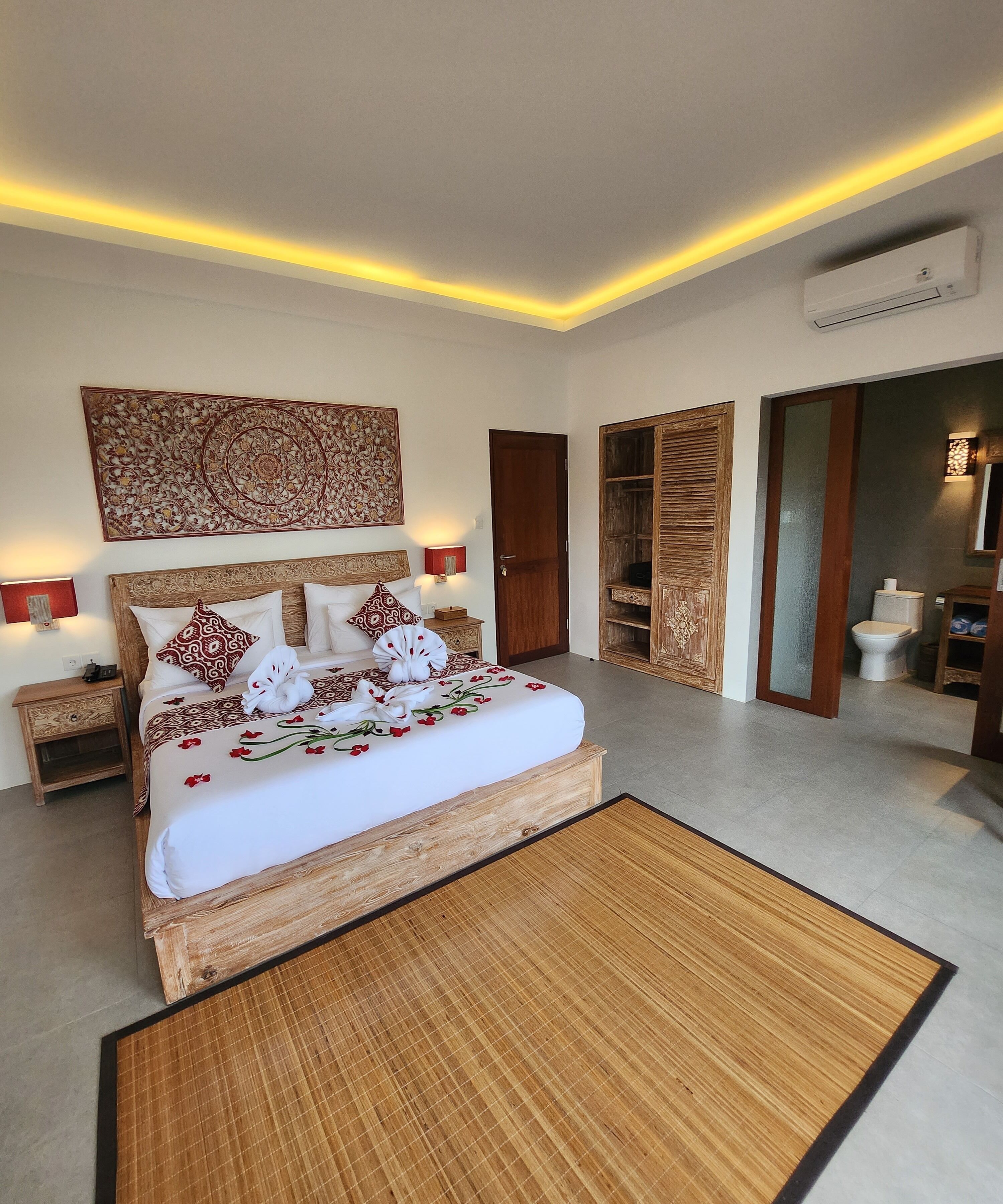 A neatly arranged bedroom with a large bed, bedside tables, a wall-mounted air conditioner, and a wooden wardrobe.
