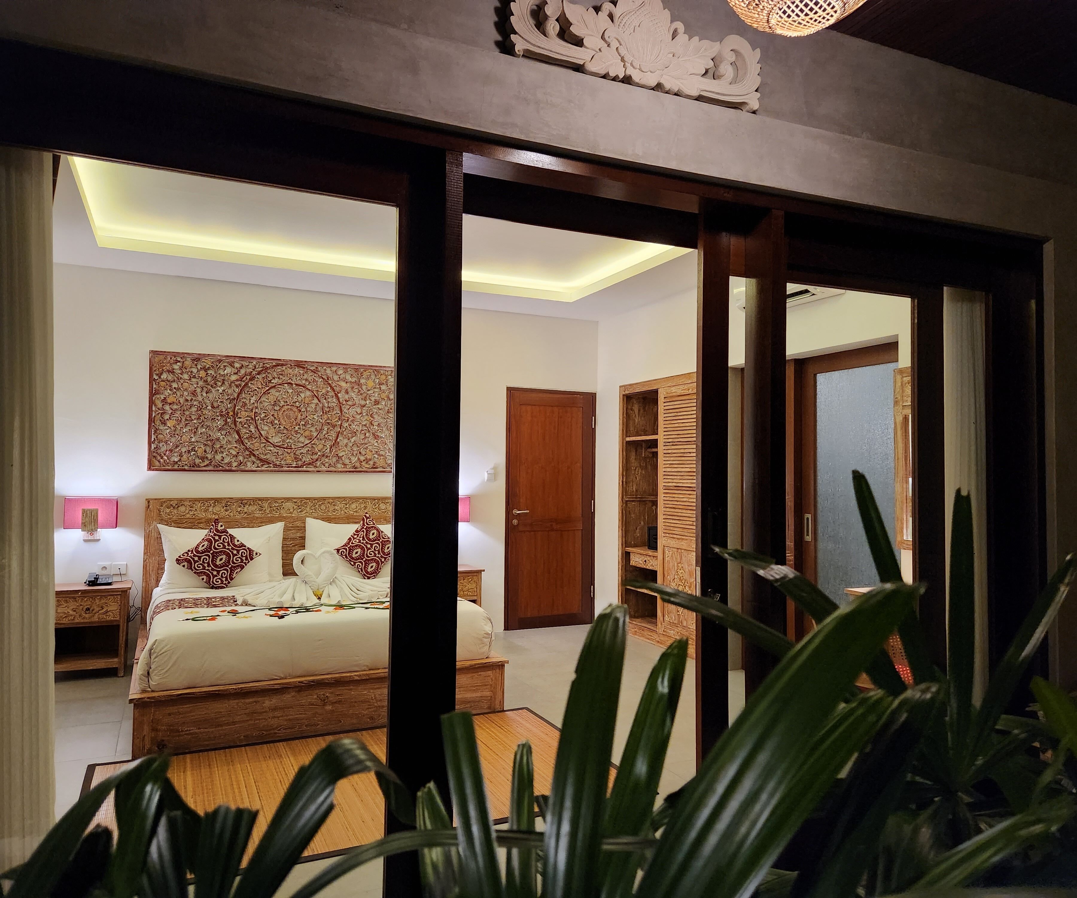 A well-lit bedroom with a large bed, a wooden headboard, and a decorative wall hanging.