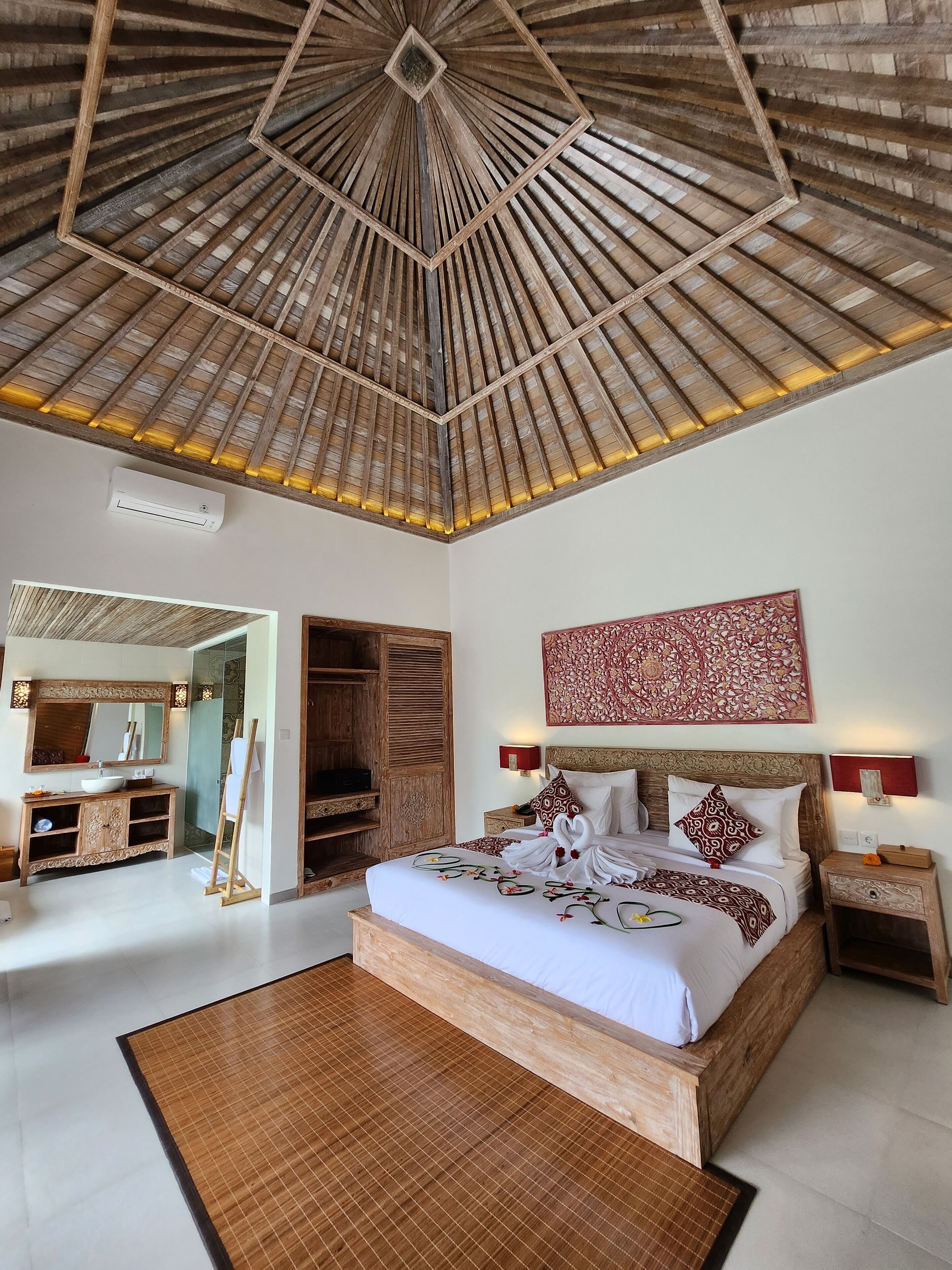 A spacious bedroom with a large bed, wooden headboard, and a ceiling fan. There is a walk-in closet and a bathroom with a large mirror and vanity.