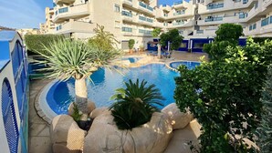 Un hotel moderno con zona de piscina rodeada de vegetación y un cielo azul despejado.