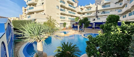 Ein modernes Hotel mit Poolbereich, umgeben von viel Grün und blauem Himmel.