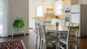 A modern kitchen with white cabinets, a built-in oven, and a refrigerator. There is a dining table with four chairs and a hanging light fixture. - Sunstreet by Interhome (Balatonoszod)