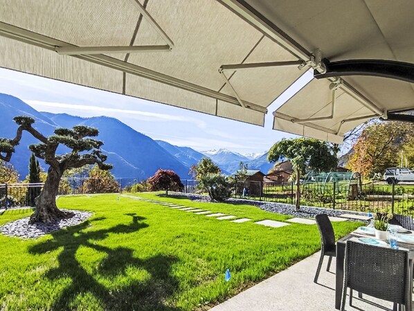 A patio with a view of mountains, a tree, and a table with chairs.