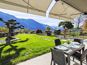 A patio with a table set for dining, a well-maintained lawn, and a view of mountains.