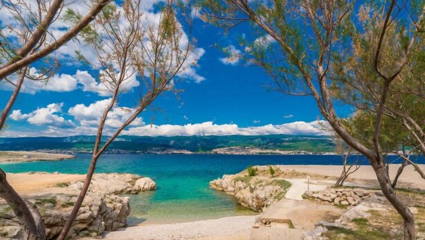 Eine Küstenlandschaft mit klarem türkisblauem Wasser, Felsformationen und einem Sandstrand.