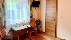Ein Zimmer mit Holzboden, einem Esstisch mit Stühlen, einem an der Wand befestigten Fernseher und einer Tür.