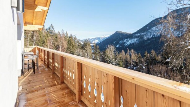 Ein hölzerner Balkon mit Blick auf verschneite Berggipfel und Bäume.