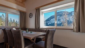 Ein Essbereich mit einem Holztisch und Stühlen, großen Fenstern mit Bergblick und einer Uhr an der Wand.