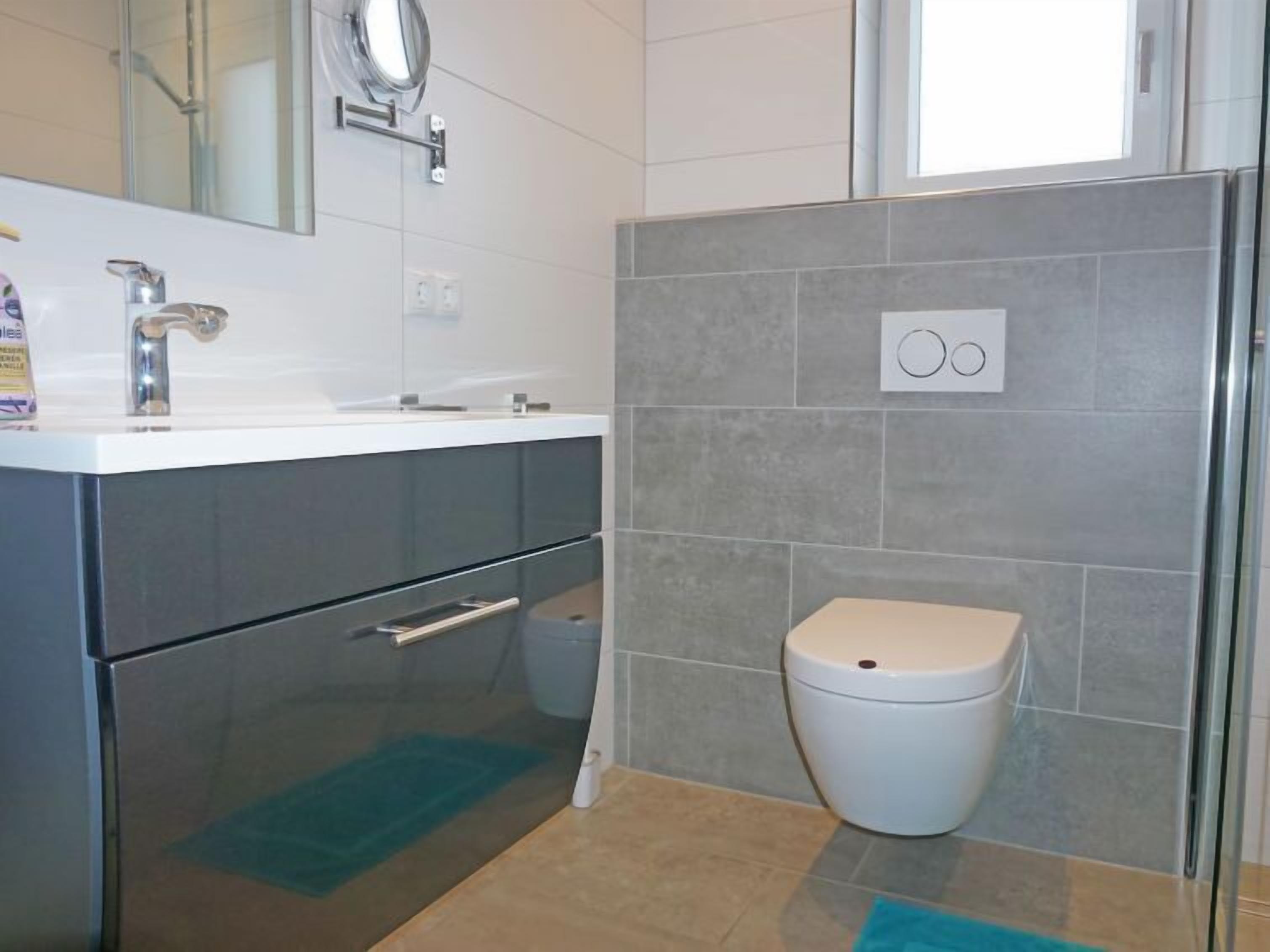 Ein modernes Badezimmer mit einem weißen Waschbecken, einem Spiegel, einer Toilette und einer Duschkabine.