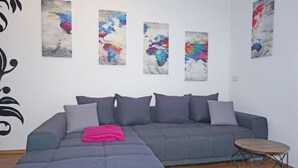Een moderne woonkamer met een grijze modulaire bank, een ronde houten salontafel en abstracte schilderijen aan de muur.