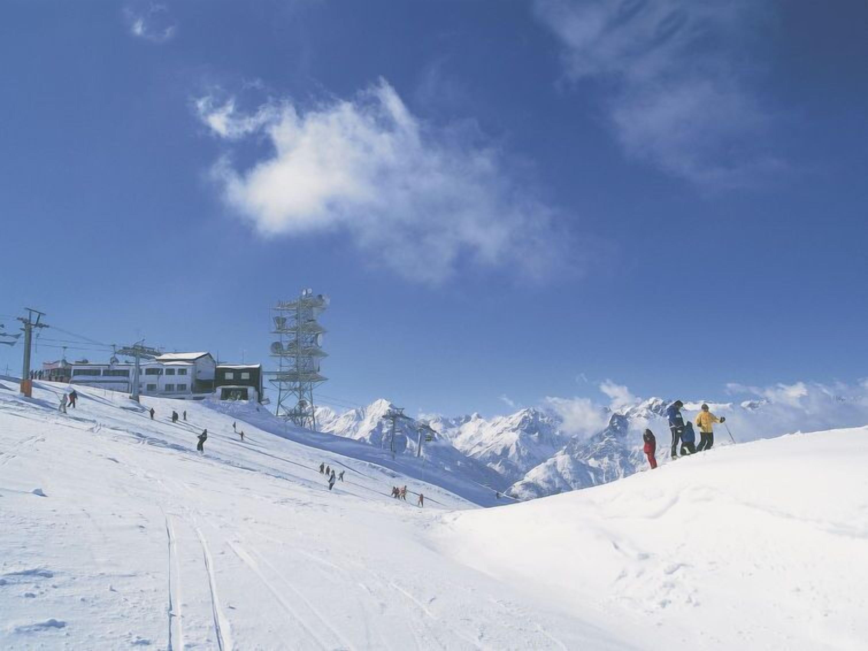 A ski slope with a building and a tall tower in the background.