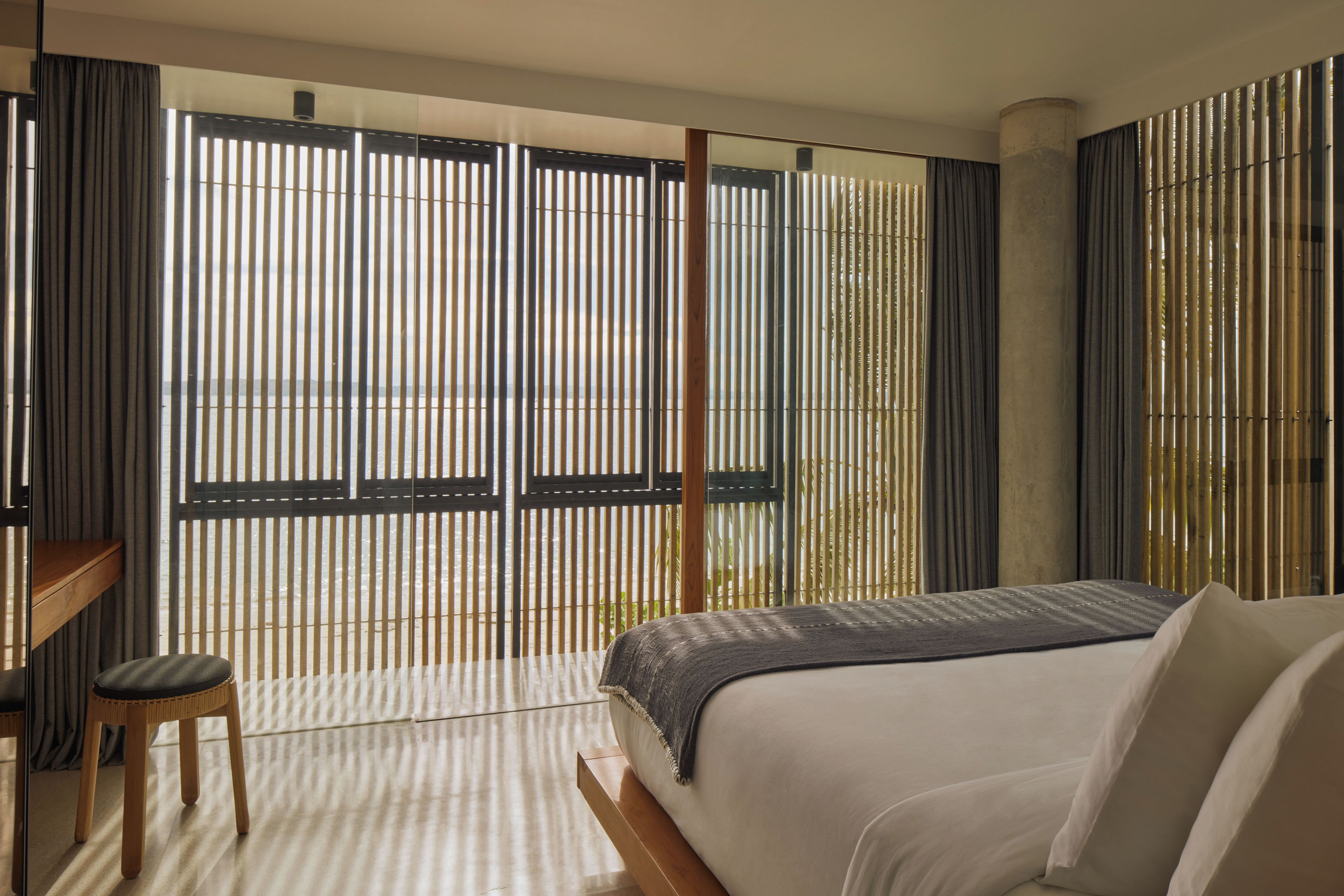 Ein modernes Hotelzimmer mit einem großen Bett, einer Holzbank und Blick durch eine Bambuswand.