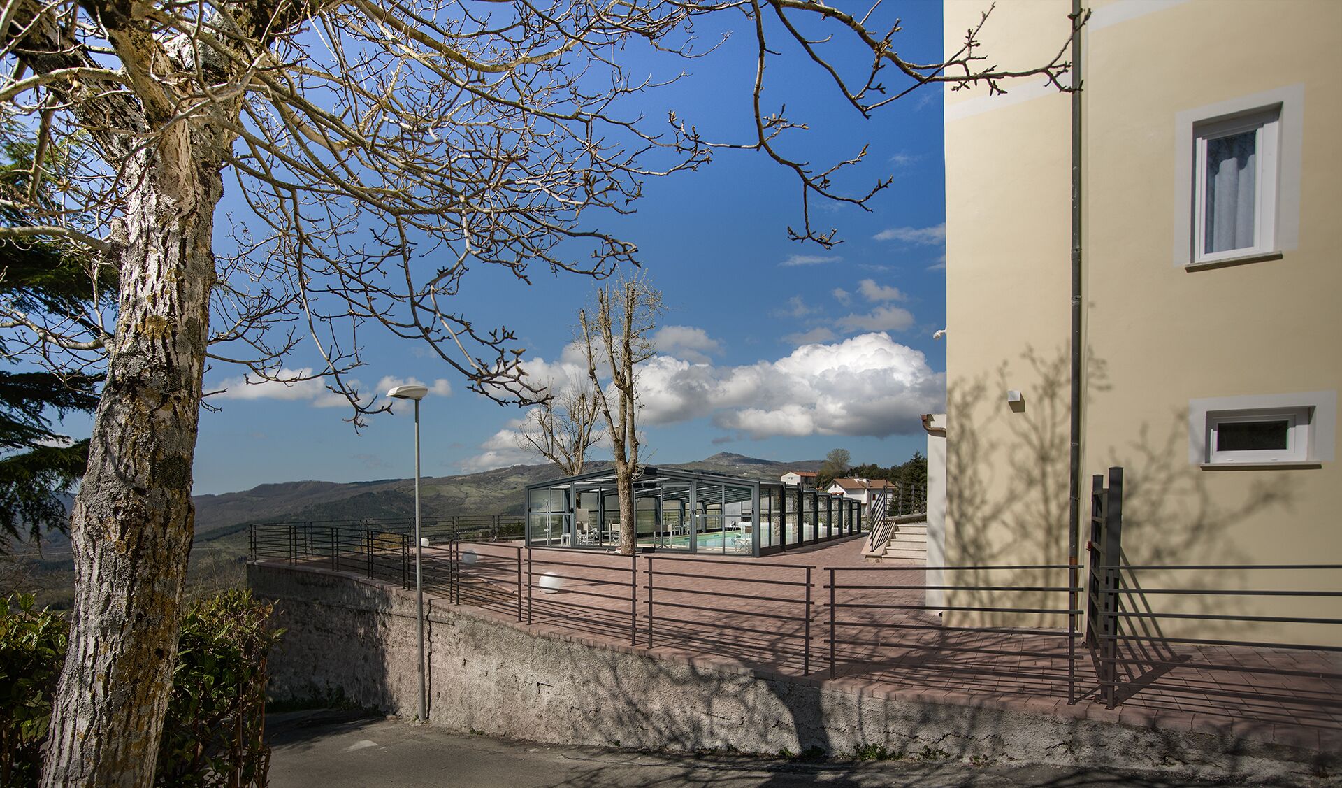 Un edificio con struttura in vetro, un vialetto lastricato e montagne sullo sfondo.
