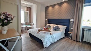 Una habitación de hotel moderna con una cama grande, mesitas de noche, una pequeña mesa de comedor y vistas al exterior.